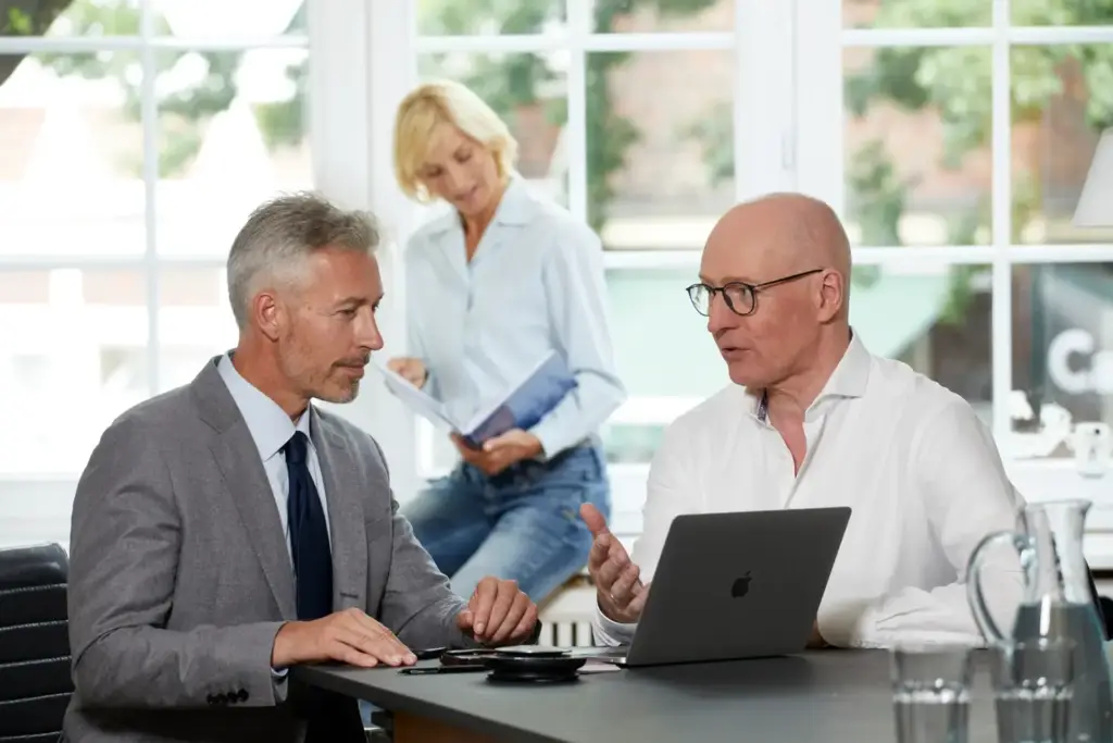 Zwei Männer sitzen am Laptop und diskutieren geschäftliche Angelegenheiten in einem modernen Bürosetting