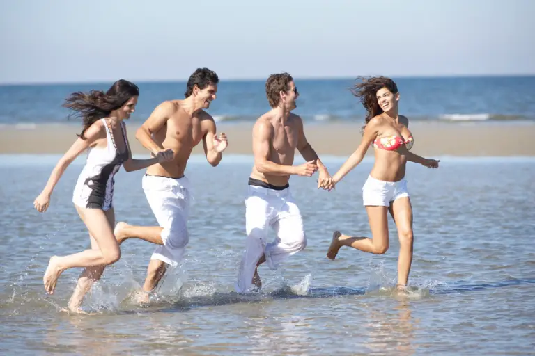 Gruppe von Freunden läuft lachend am Strand ins Meer